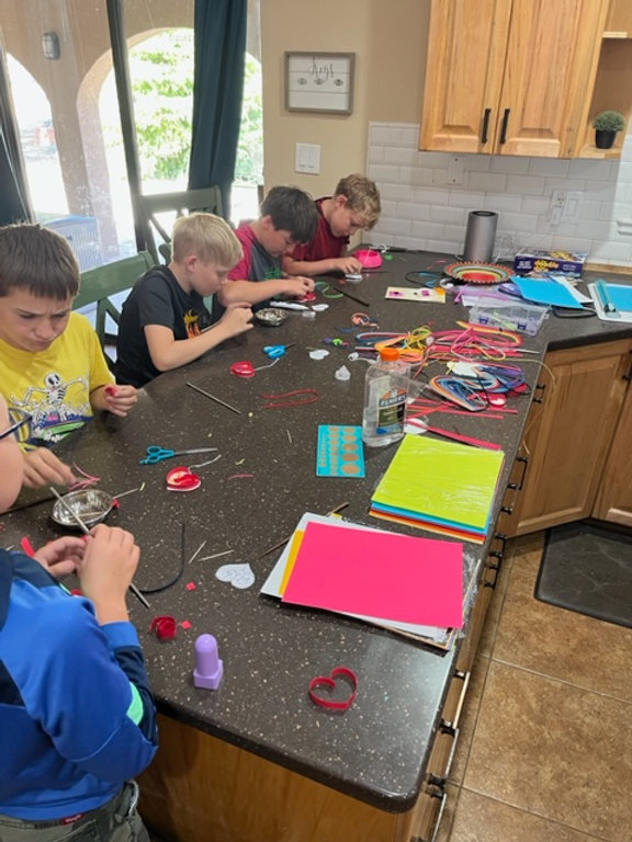 Version 1: Children engaged in creative activities, crafting at the kitchen table. Version 2: Kids showcasing their artistic skills while crafting at the kitchen table. Version 3: Youngsters immersed in crafting projects, gathered around the kitchen table.