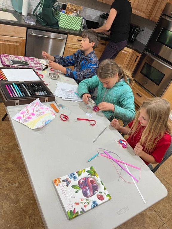 Version 1: Children engaged in creative activities, crafting at the kitchen table. Version 2: Kids showcasing their artistic skills while crafting at the kitchen table. Version 3: Youngsters immersed in crafting projects, gathered around the kitchen table.