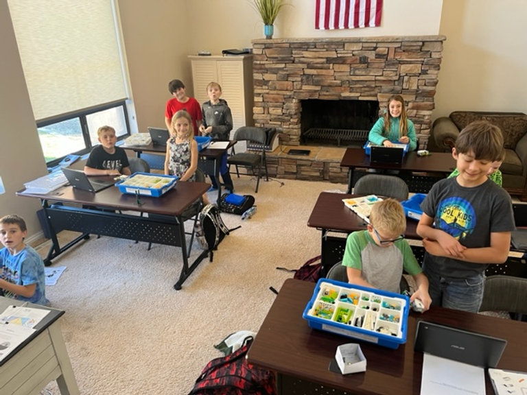 A group of children sitting at desks with laptops, engaged in learning activities.