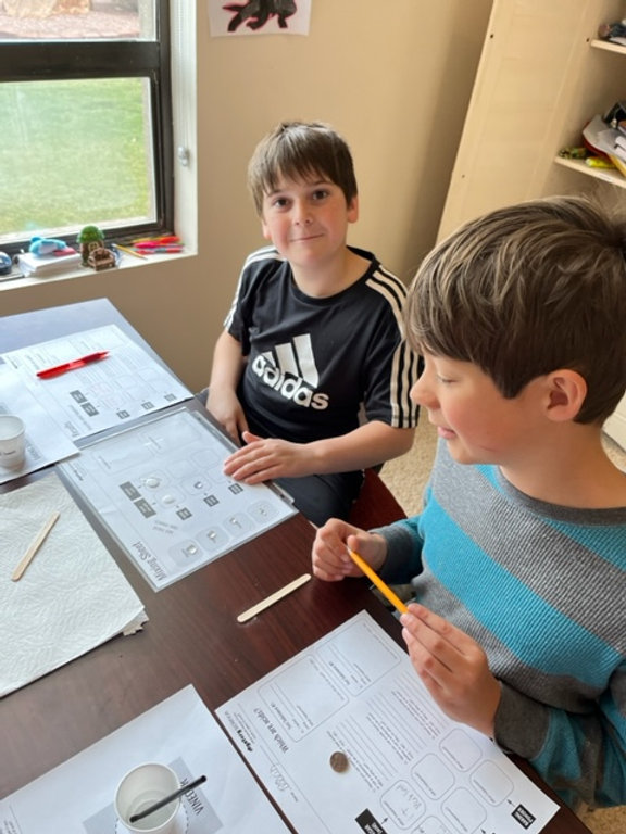Two boys sitting at a table, engrossed in their work, using paper and pencils to create something artistic.